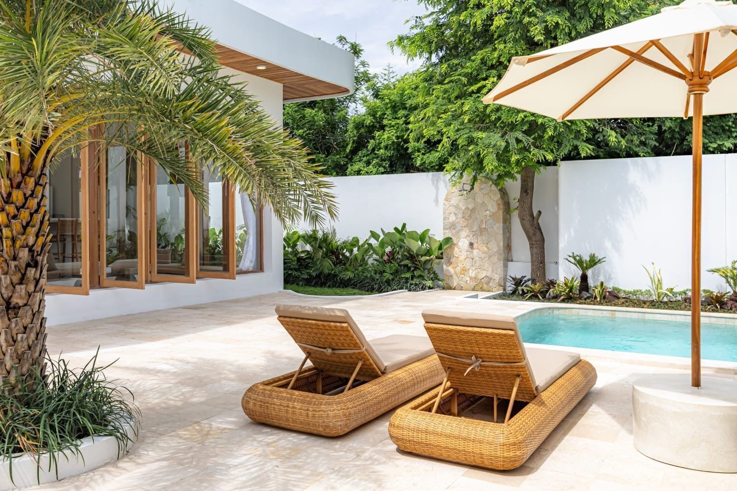 A modern outdoor pool area with two wicker lounge chairs and a large umbrella.