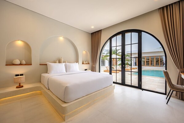 Un dormitorio con una cama grande, un escritorio, una silla, vistas a la piscina y una pared curva.