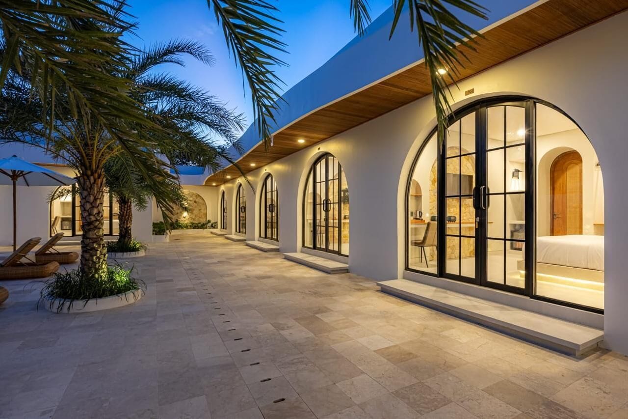 A modern hotel with a covered outdoor area, palm trees, and a well-lit interior.