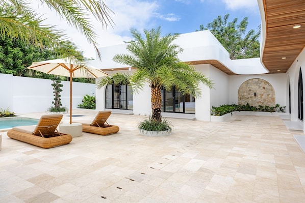 A modern outdoor patio with a pool, lounge chairs, and a palm tree.