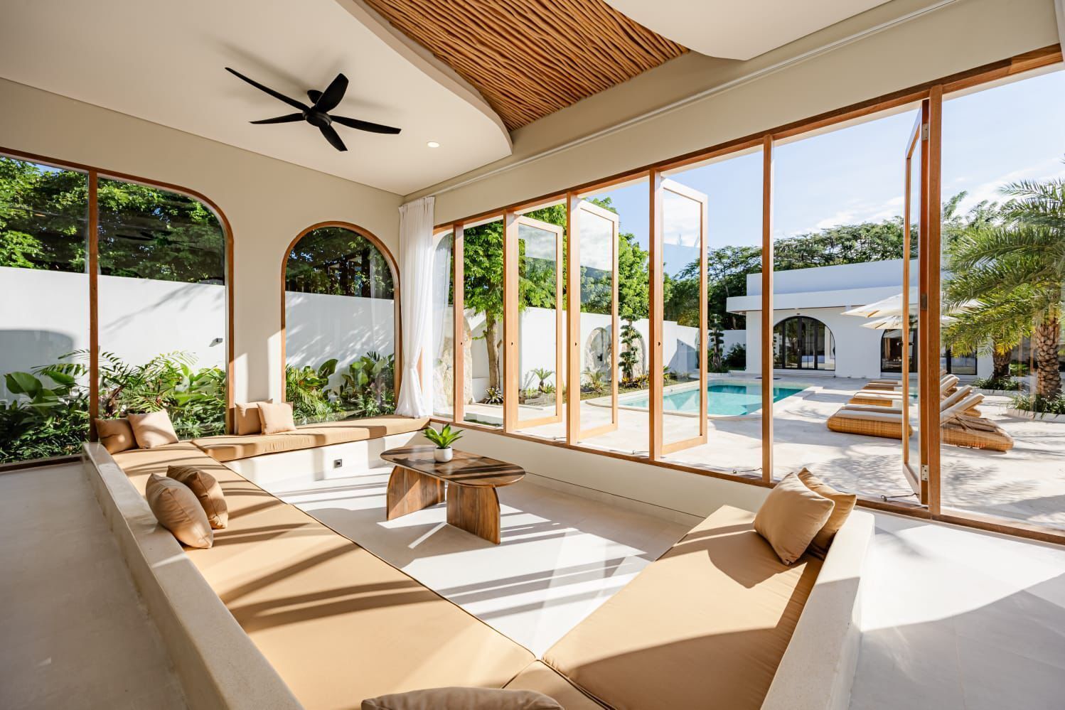 A modern outdoor lounge area with a pool, large windows, and a ceiling fan.