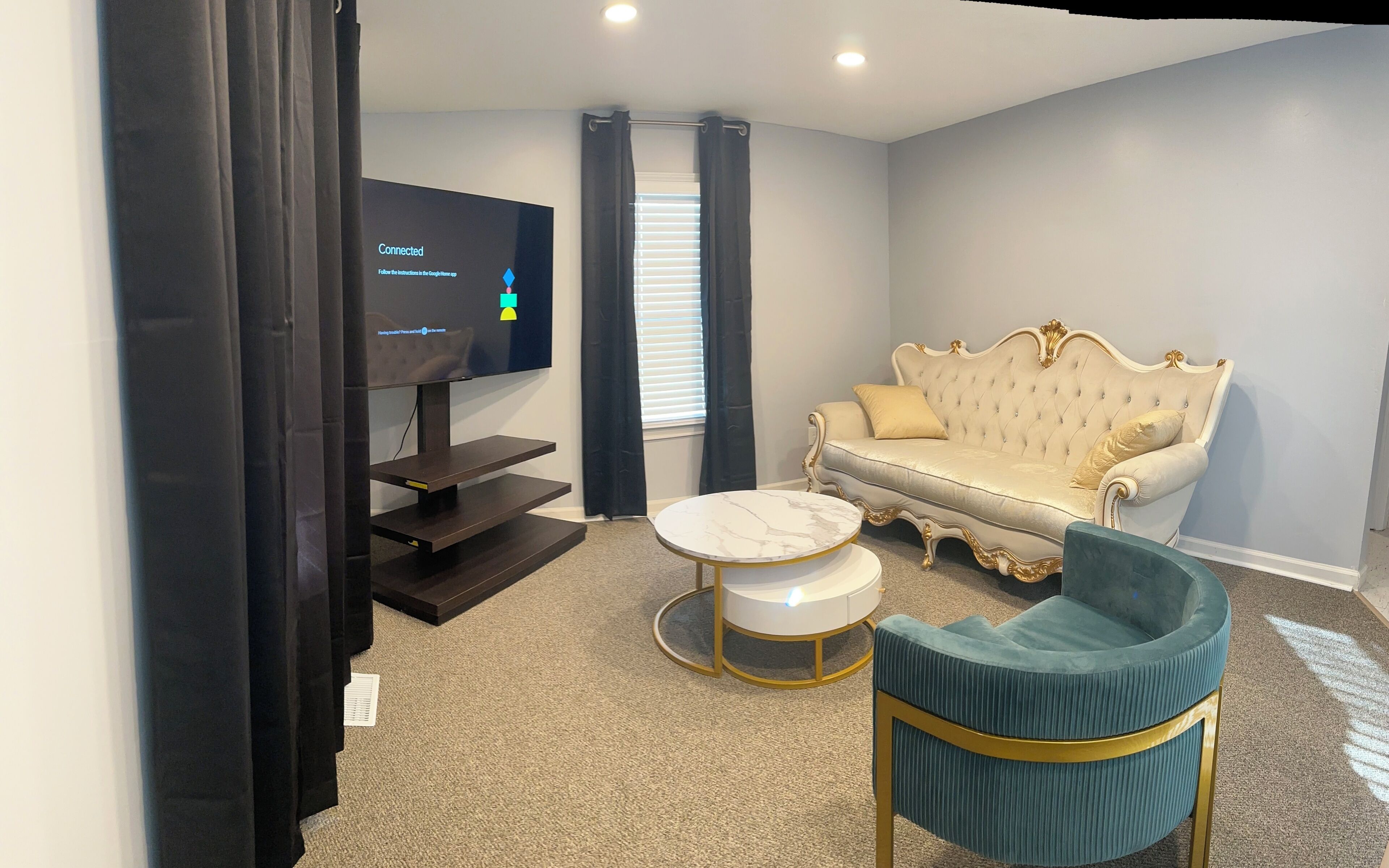 Een woonkamer met een televisie, een bank, een rond bijzettafeltje en een teal fauteuil.