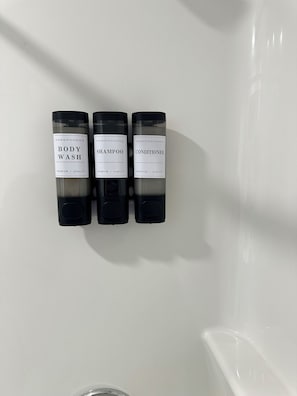 Three bottles of body wash, shampoo, and conditioner on a white wall.