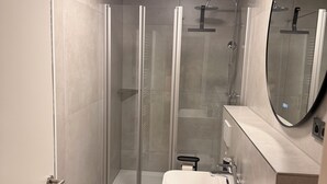 A modern bathroom with a glass-enclosed shower, a sink, and a mirror.