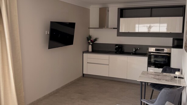 A modern kitchen with a flat-screen TV, built-in oven, and a dining area with a table and chairs.