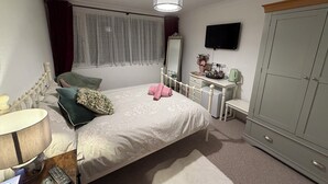 Ein Schlafzimmer mit Bett, Nachttisch, Lampe, Kommode, Spiegel, Kleiderschrank und Fernseher an der Wand.