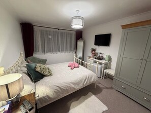 A bedroom with a bed, bedside table, lamp, dresser, mirror, wardrobe, and a television on the wall. - A lovely double room with wardrobe, fridge, WiFI (Exeter)
