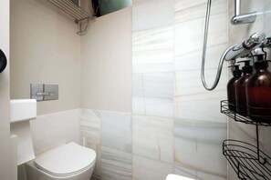 A bathroom with a toilet, a shower, and a towel rack. - Cosy Outhouse in Clapham | Zone 2 | BeeMyGuest® (London)
