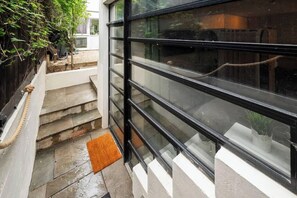 A modern building with a glass facade, a staircase leading to a door, and a small outdoor area with steps and a doormat. - Cosy Outhouse in Clapham | Zone 2 | BeeMyGuest® (London)