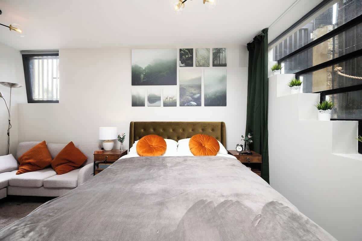 Un dormitorio moderno con una cama grande, un sofá, una mesita de noche con lámpara y una pared decorada con múltiples cuadros.