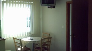 Ein Zimmer mit einem runden Tisch, vier Stühlen, einem an der Wand befestigten Fernseher und einer Tür.