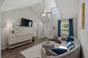 A spacious living room with a high ceiling, a ceiling fan, a flat-screen TV, a white sofa, a round coffee table, and a large window with blue curtains. - 3-bedroom Home in Historic Gallatin PICTURES COMING SOON! (Gallatin)
