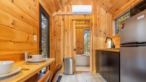 A wooden cabin interior with a dining table, chairs, a sink, and a refrigerator.