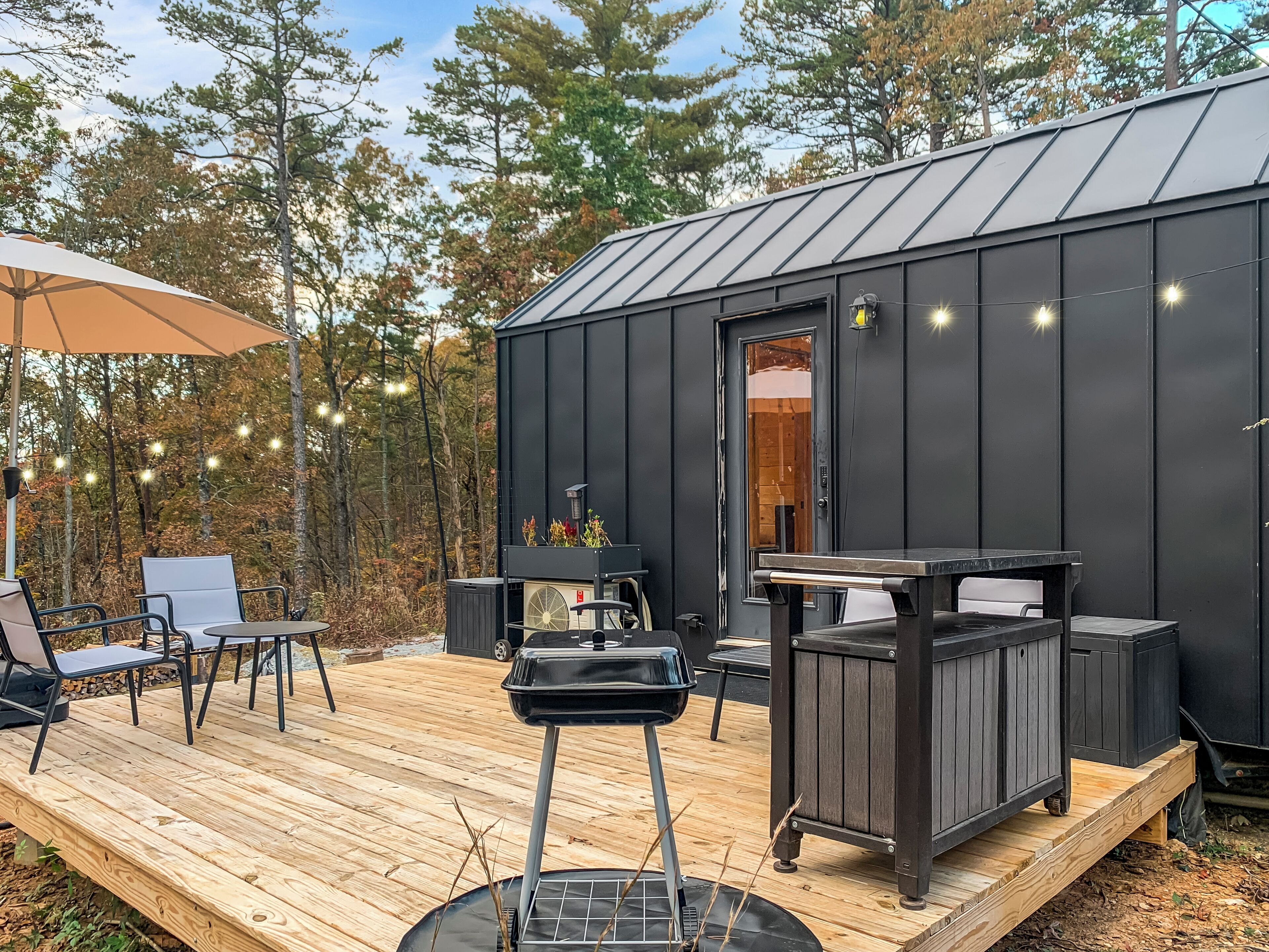 A wooden deck with outdoor furniture, a grill, and string lights.