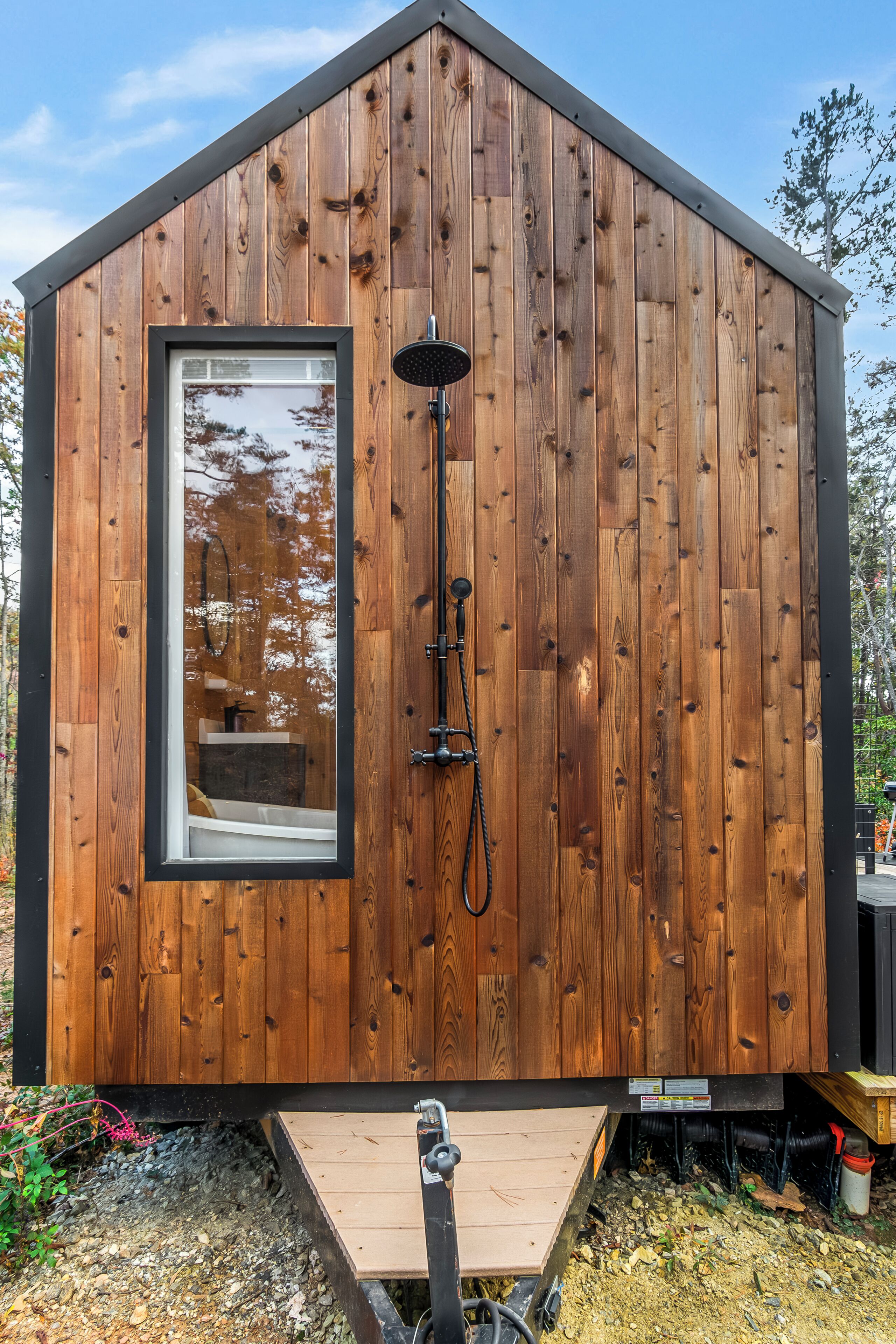 A wooden cabin with a window, a shower, and a small deck.