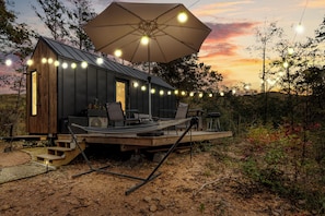 Une petite cabane dotée d’une terrasse, de sièges d’extérieur et de guirlandes lumineuses.