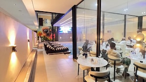 Un couloir d’hôtel moderne, doté d’un espace salon, de tables et d’une grande paroi vitrée donnant sur la salle à manger.