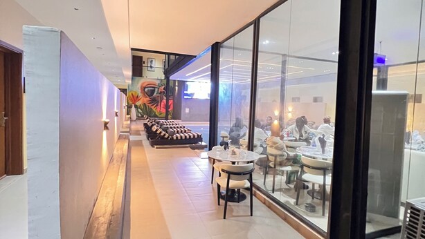 Un hall d’hôtel moderne avec un long couloir, un espace salon et un mur de verre donnant sur la salle à manger.