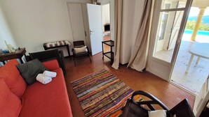 A room with a red sofa, a small table with a lamp, a chair, a colorful rug, and a view of the ocean through a large window. - House with pool and garden in Les Issambres (Roquebrune-sur-Argens)