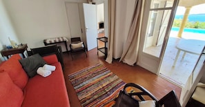 Ein Zimmer mit einem roten Sofa, einem kleinen Tisch mit einer Lampe, einem Sessel, einem bunten Teppich und Meerblick durch ein großes Fenster.