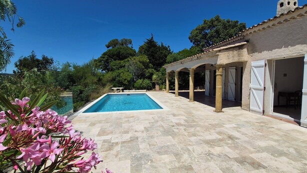 A pool with a tiled deck, a covered patio area, and a building with open doors. - House with pool and garden in Les Issambres (Roquebrune-sur-Argens)