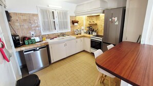 A compact kitchen with a dishwasher, stove, refrigerator, and a wooden dining table. - House with pool and garden in Les Issambres (Roquebrune-sur-Argens)