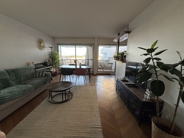 Ein Wohnzimmer mit einer Couch, einem Esstisch, Stühlen, einem Fernseher und einem Balkon mit Blick.