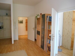 An open door leading to a room with a wooden floor, a bookshelf, and a kitchen area visible in the background. - To "Senckenberg IV for Two" by Satischni. Apartment with parking and a balcony (Görlitz)