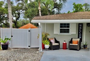 A house with a 'WELCOME' sign, a covered patio, a covered patio, and a gravel driveway.