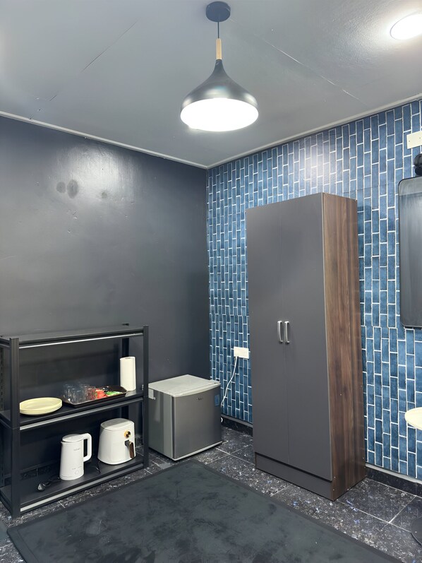 A modern bathroom with a dark wall, a blue-tiled shower area, a wooden wardrobe, and a shelf with toiletries.