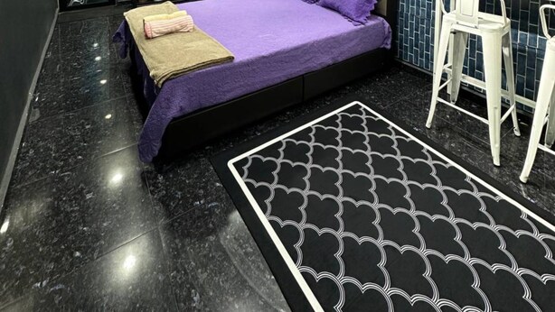 A modern bedroom with a bed, a desk, and a patterned rug.