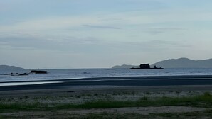 A beach with a clear sky, calm sea, and distant landforms.