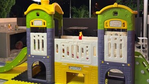 A children's play area with a castle-themed play structure, a slide, and a covered outdoor space with a metal roof and hanging lights.