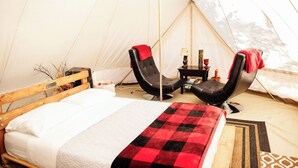 Ein Zelt mit einem Bett, zwei Stühlen, einem kleinen Tisch und einer Lampe.