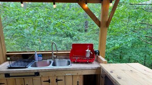 Ein rustikales Holzhaus mit Küchenbereich, ausgestattet mit einem Spülbecken, einem roten Transportkocher und einem Fenster mit Blick auf einen Wald.