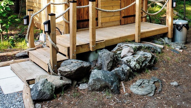 Eine Holzhütte mit Veranda, Seilabsperrung und Mülleimer.