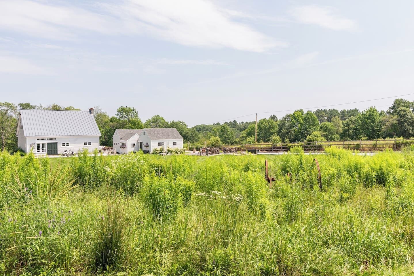 A white farmhouse with a metal roof, surrounded by lush green fields and trees in the background.