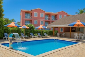 A swimming pool with lounge chairs and umbrellas, a building with balconies, and a thatched-roof structure. - Petit nid d'amour in Ponta Negra (Natal)