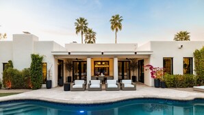Una casa moderna con piscina, mobiliario exterior y palmeras.