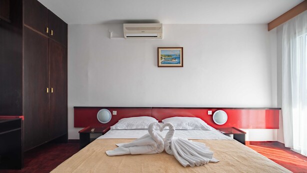 Ein Hotelzimmer mit einem Bett, einer Wand-Klimaanlage, einem gerahmten Bild und einem roten Kopfteil.