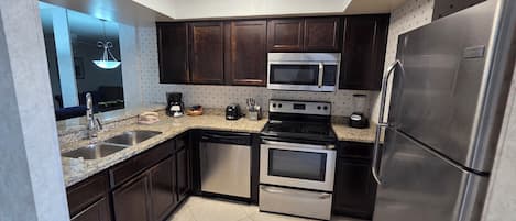 A modern kitchen with dark wooden cabinets, stainless steel appliances, a granite countertop, and a skylight.