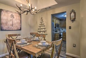 A dining area with a wooden table set for four, a chandelier, a Christmas tree, and a painting on the wall. - Broken Antler at Sugar Top — Grandfather Mountain Views, Indoor Pool & Hot Tub (Sugar Mountain)