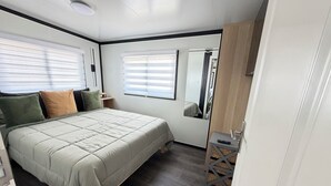 Ein Schlafzimmer mit einem Bett, einem Nachttisch, einem Spiegel und einem Fenster mit Jalousien.