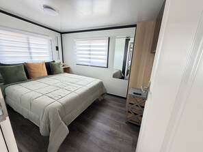 Un dormitorio con cama, mesita de noche, espejo y ventana con persianas.