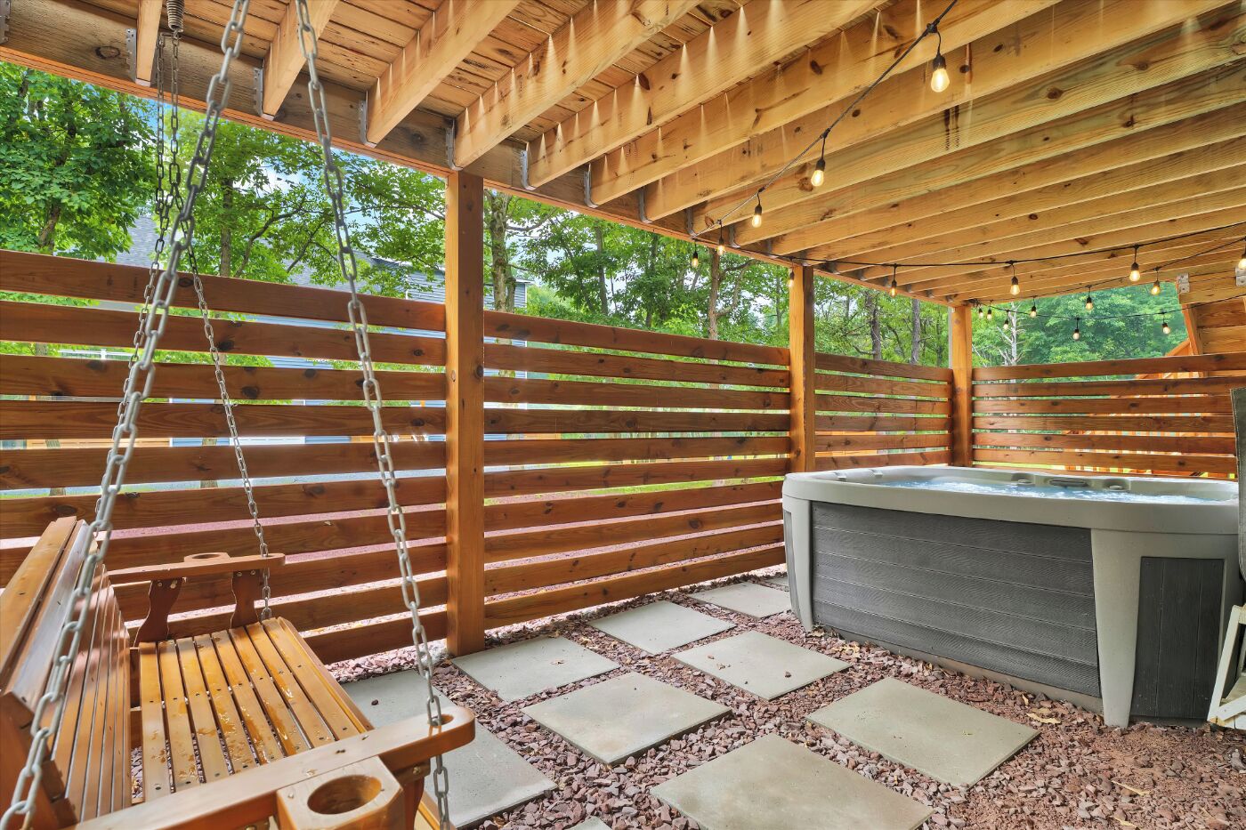 Un patio exterior con jacuzzi, una mecedora de madera y una pérgola.