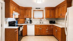 Een keuken met houten kastjes, een vaatwasser, een fornuis, een magnetron en een koelkast.