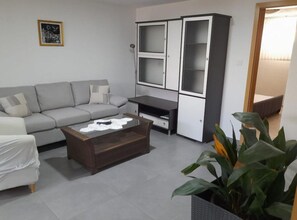 Ein Wohnzimmer mit grauem Sofa, einem Holztisch, einer Vitrine mit Glastüren und einer Topfpflanze.