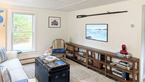 Un salon chaleureux avec un canapé, une table basse en bois, une bibliothèque, un tableau encadré et une fenêtre donnant sur un paysage verdoyant.