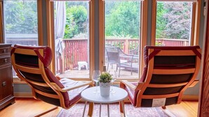 Een kamer met twee stoelen, een klein tafeltje en uitzicht op een houten terras en groen.