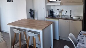 Eine kleine Küche mit Holztisch, zwei Barhocker, einer Mikrowelle, einer Kaffeemaschine und einem Spülbecken.